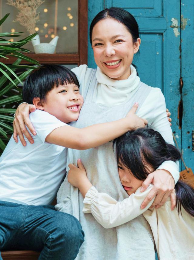 A warm family moment showing a mother and two children sharing a loving embrace in front of a vintage turquoise door